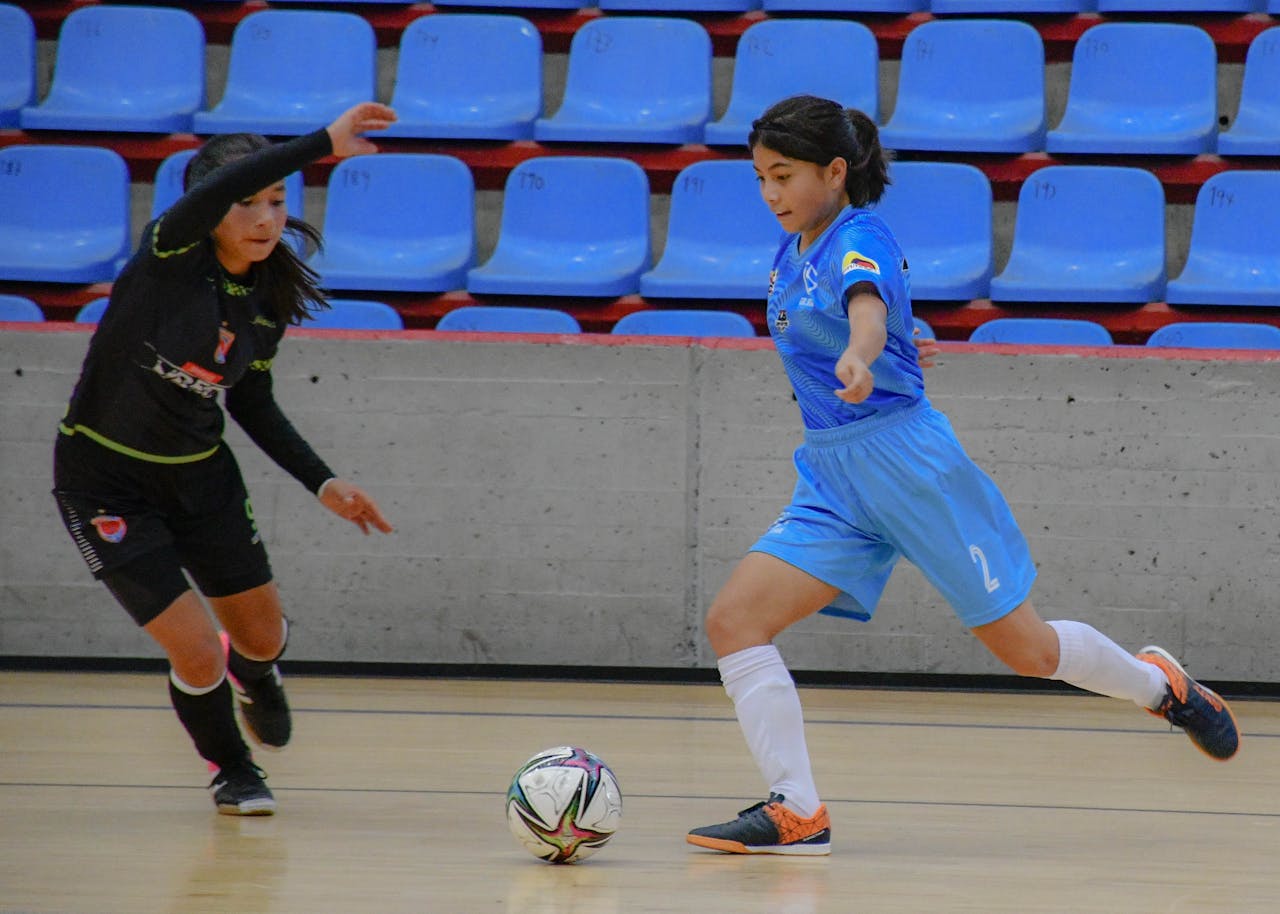 Action shot of teenage girls playing futsal indoors, showcasing teamwork and competition.